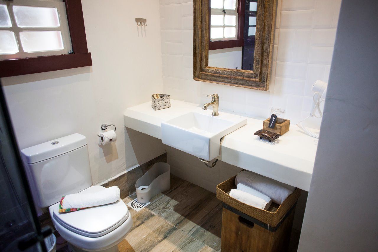 Une salle de bain avec des toilettes blanches, deux lavabos, un miroir et un panier en bois.