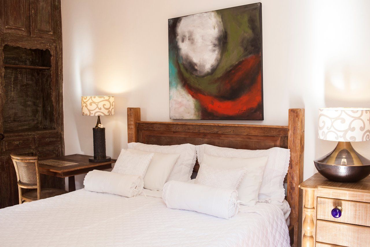 Cama bem arrumada com roupa de cama branca, cabeceira de madeira e uma pintura abstrata moderna na parede.