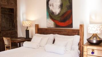 Cama bem arrumada com roupa de cama branca, cabeceira de madeira e uma pintura abstrata moderna na parede.