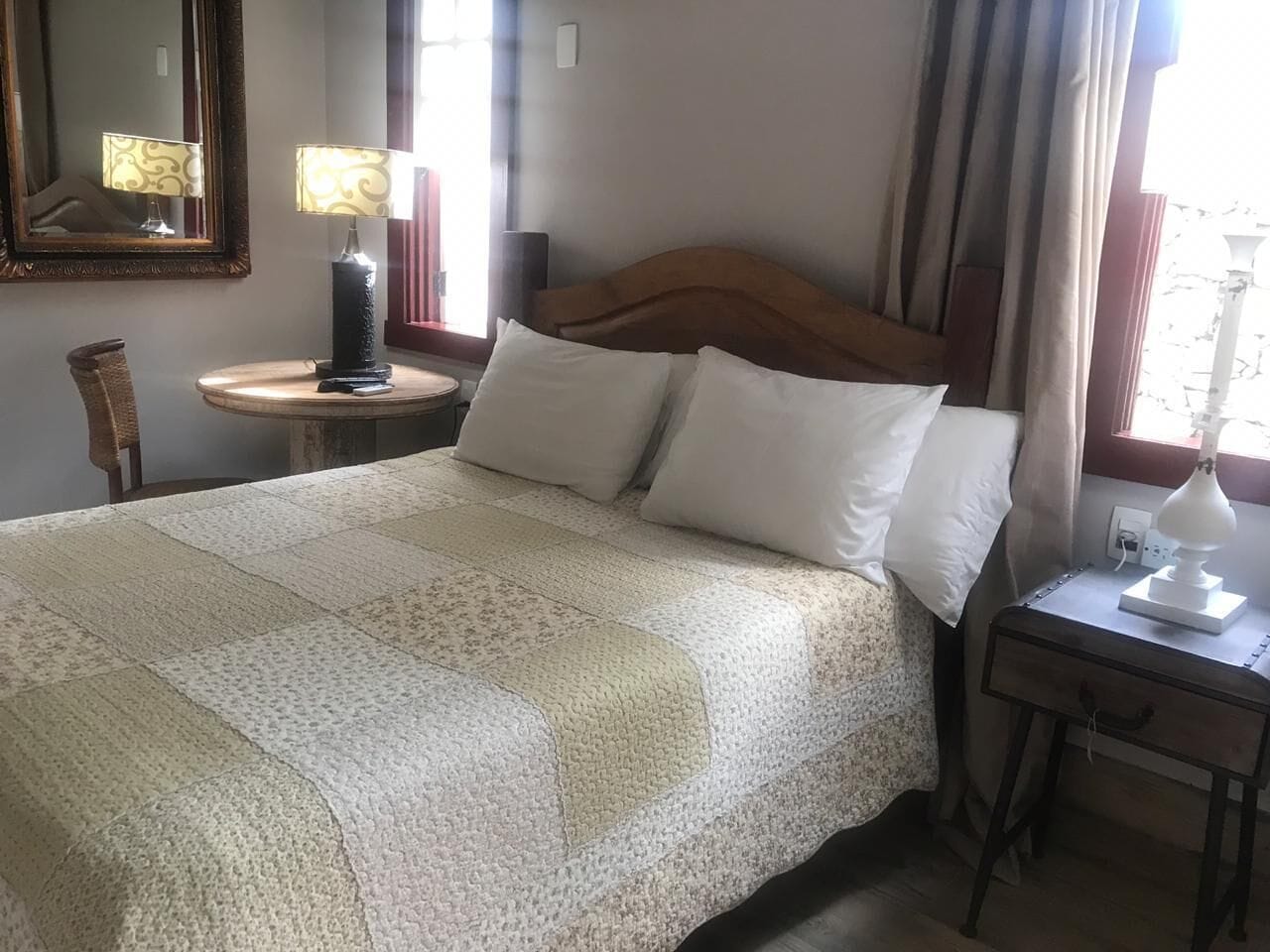 Ein ordentlich bezogenes Bett mit einer gesteppten Decke, ein Nachttisch mit Lampe und ein Sessel.