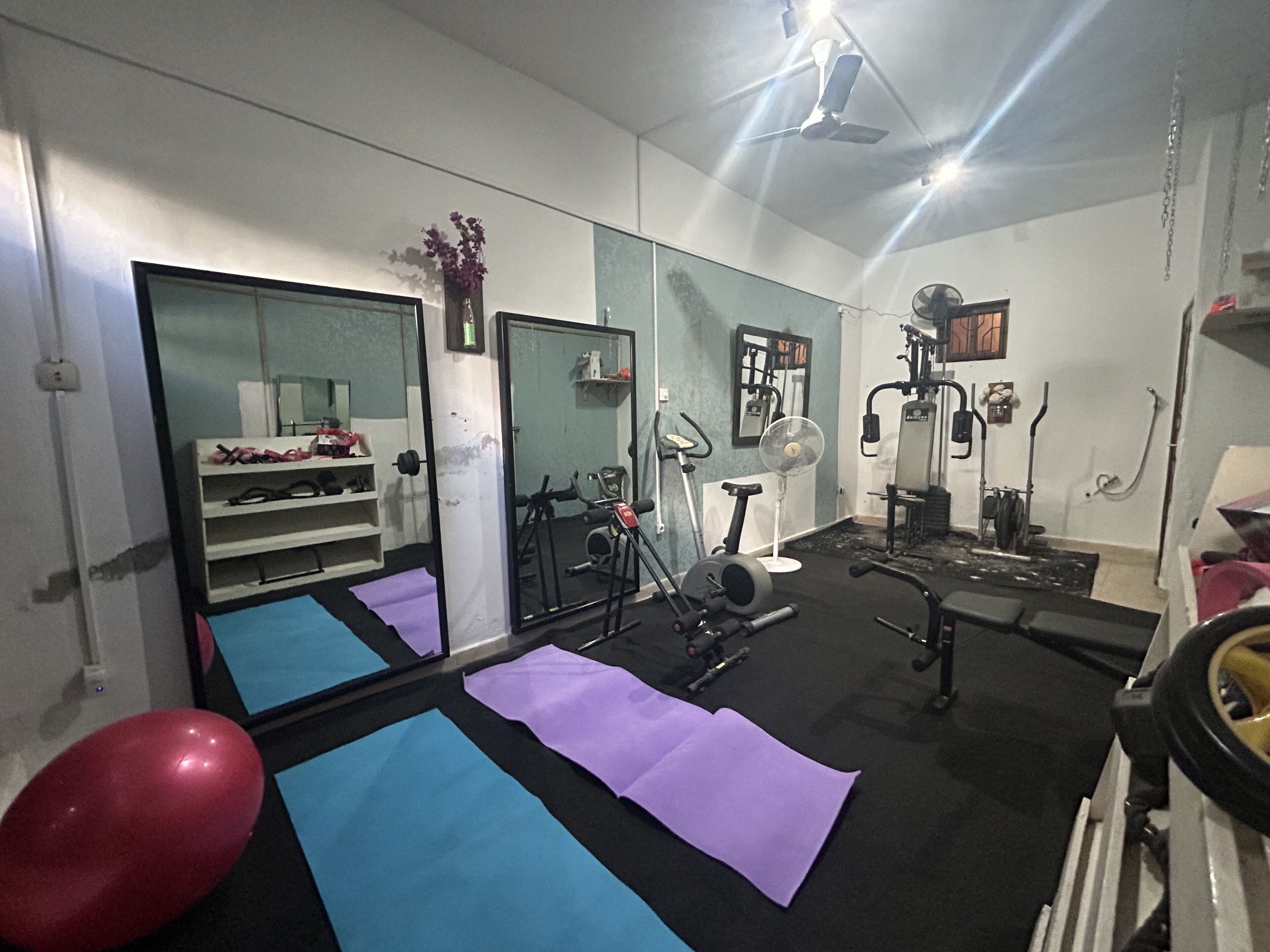 Une salle de sport équipée de matériel d’exercice, de tapis de yoga et d’un grand miroir.