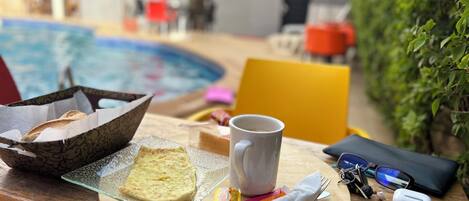 Un vassoio per la colazione con pane tostato, una tazza e un tovagliolo su un tavolo di legno vicino a una piscina.