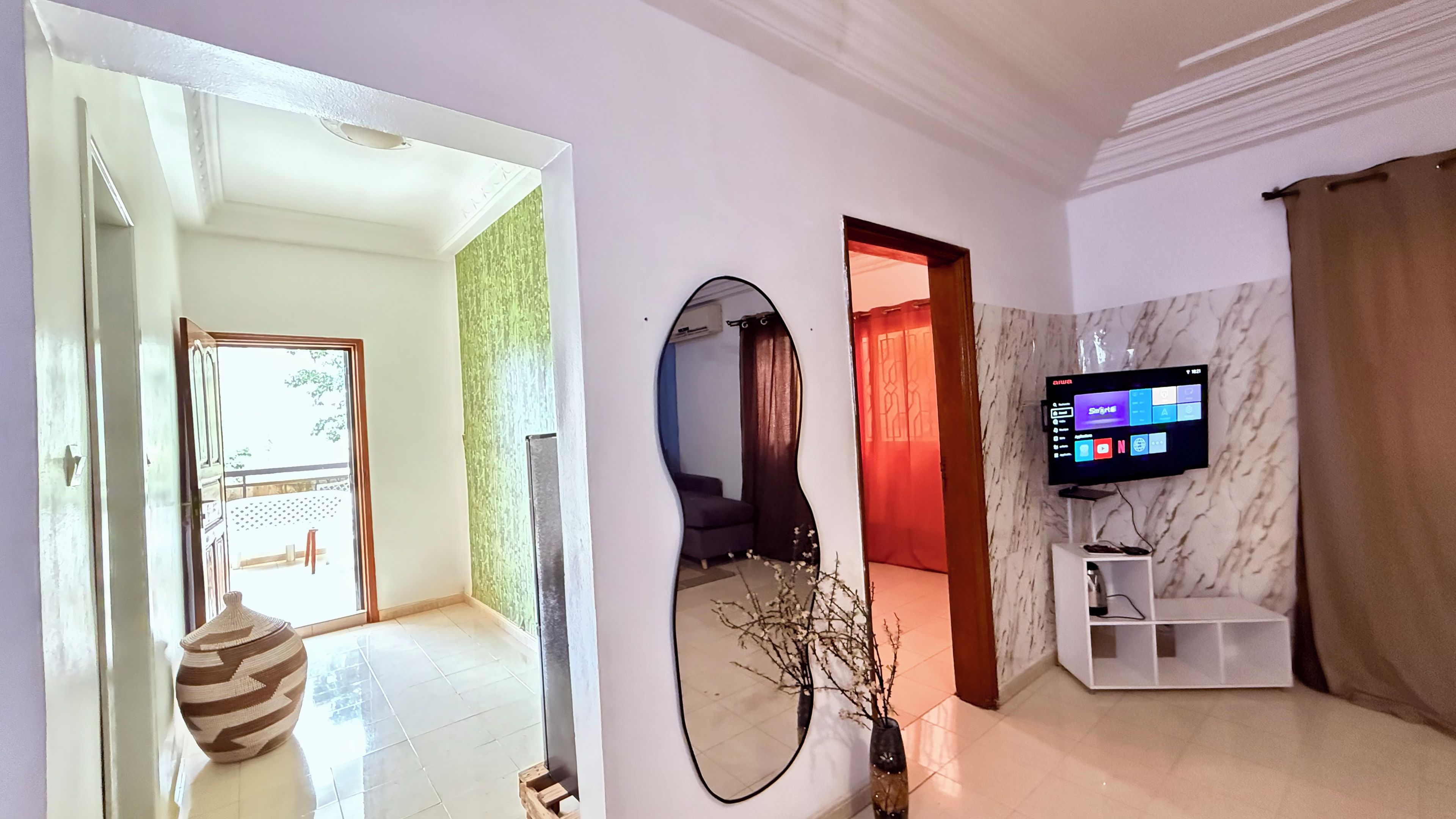 A modern living room with a flat-screen TV, a large mirror, and a decorative vase.