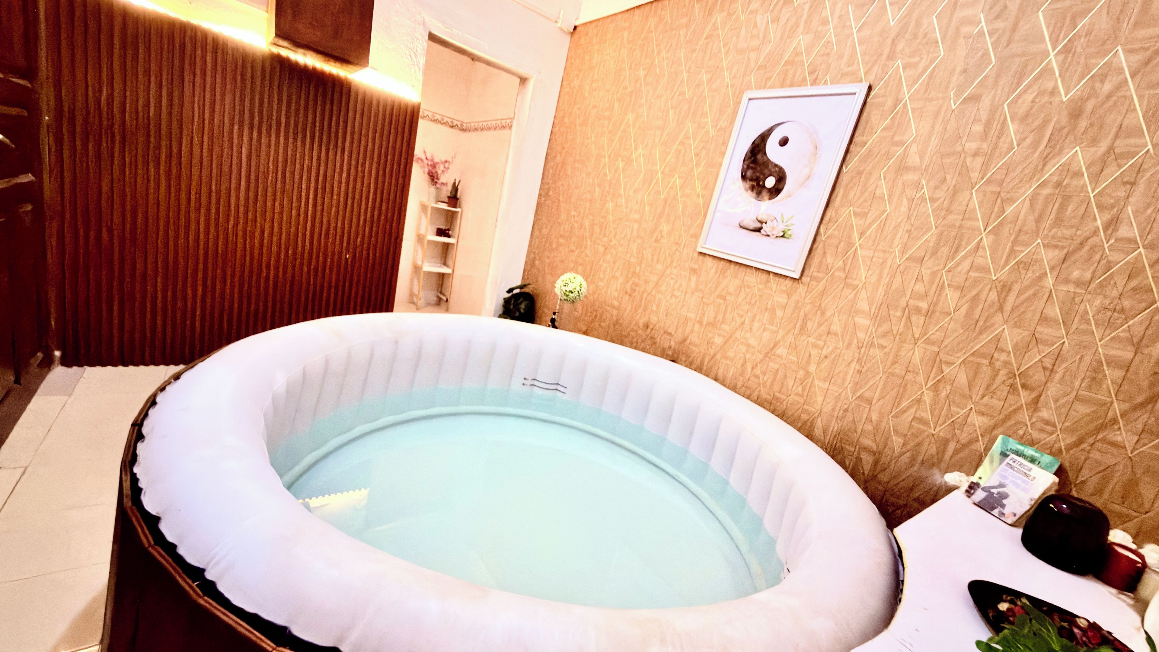 A room with a large inflatable hot tub, a framed yin-yang symbol on the wall, and a small shelf with items.