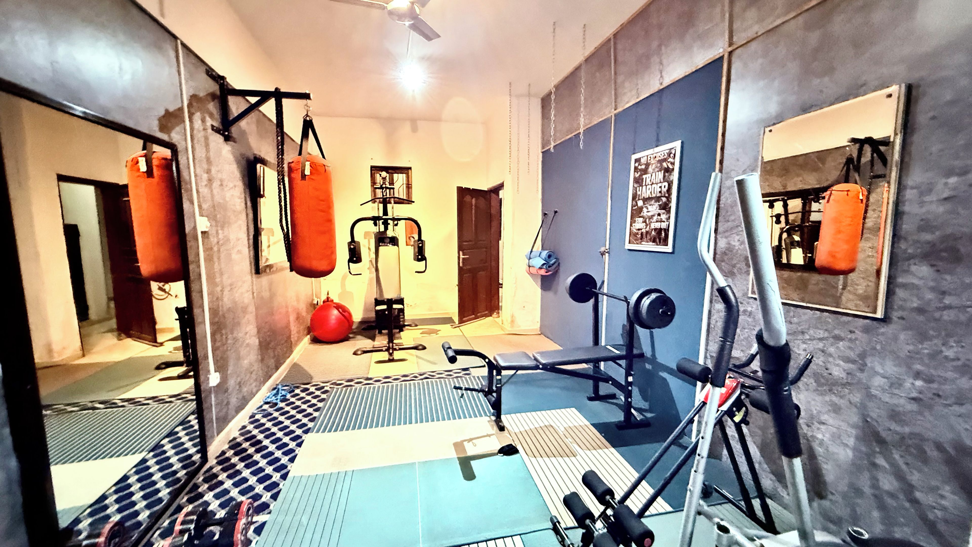 A gym with various exercise equipment, a punching bag, and a mirror on the wall.