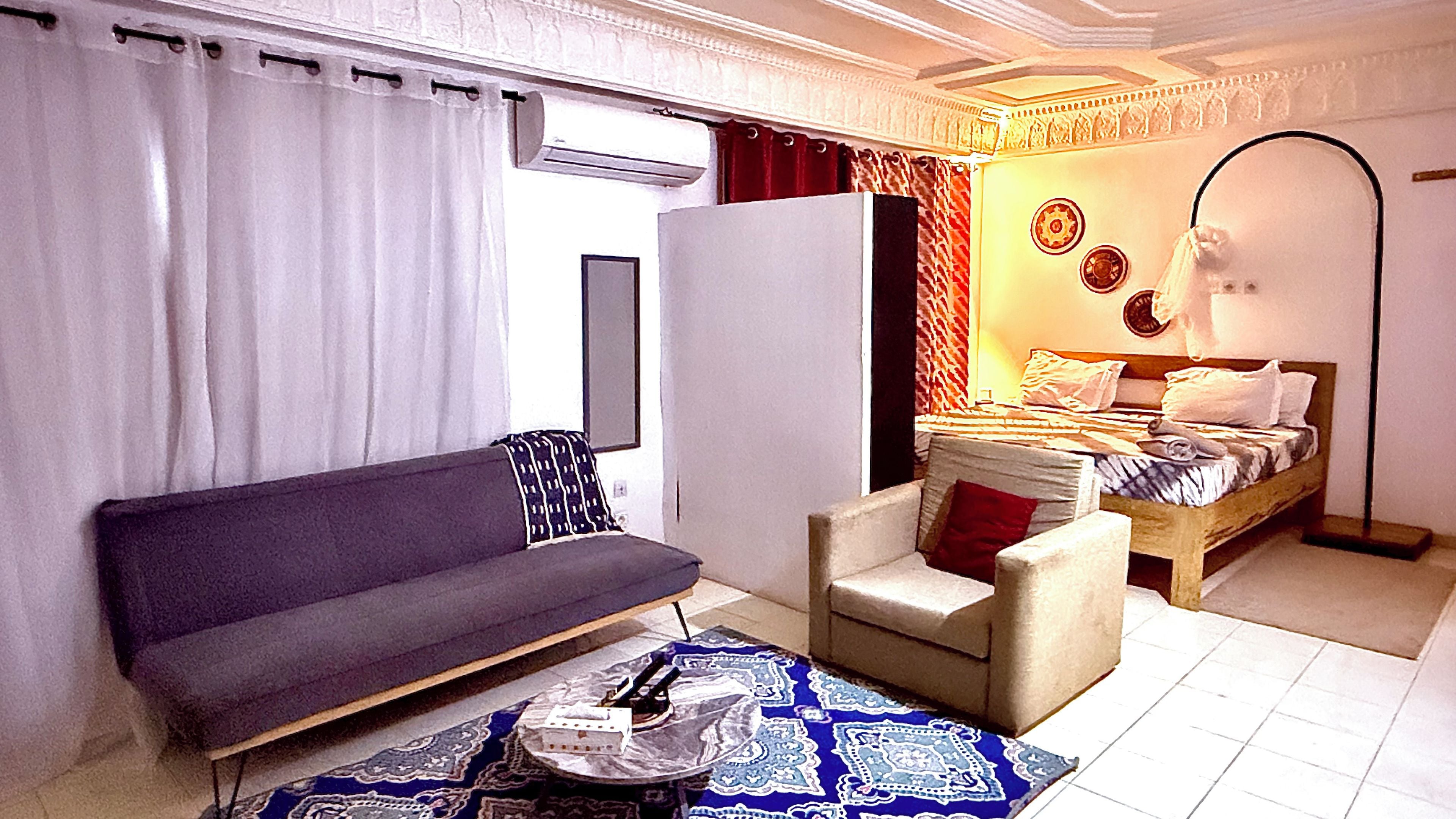 Un dormitorio moderno con sofá, sillón, cama y espejo.