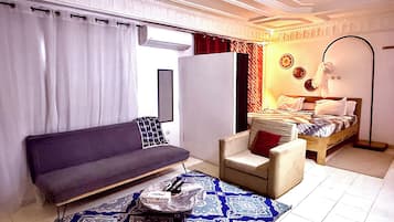 Un dormitorio moderno con sofá, sillón, cama y espejo.