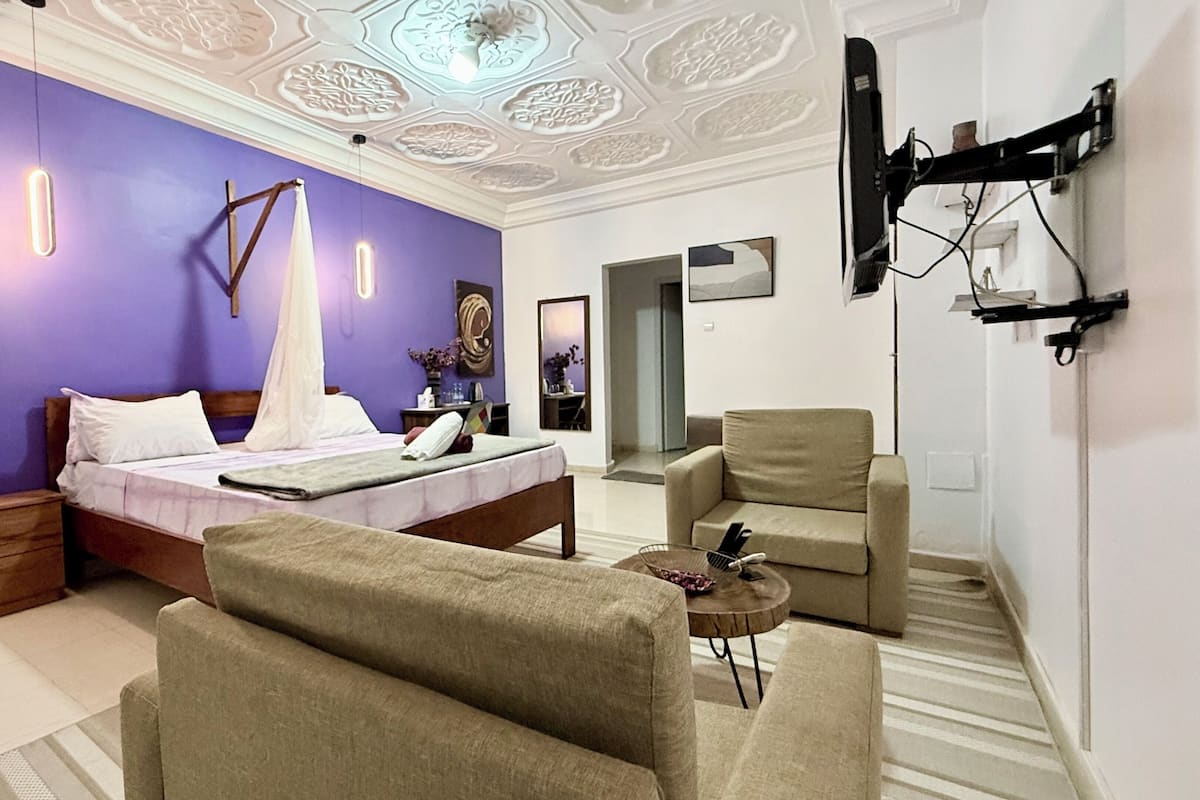 A modern bedroom with a bed, a chair, a small table, and a TV mounted on the wall.