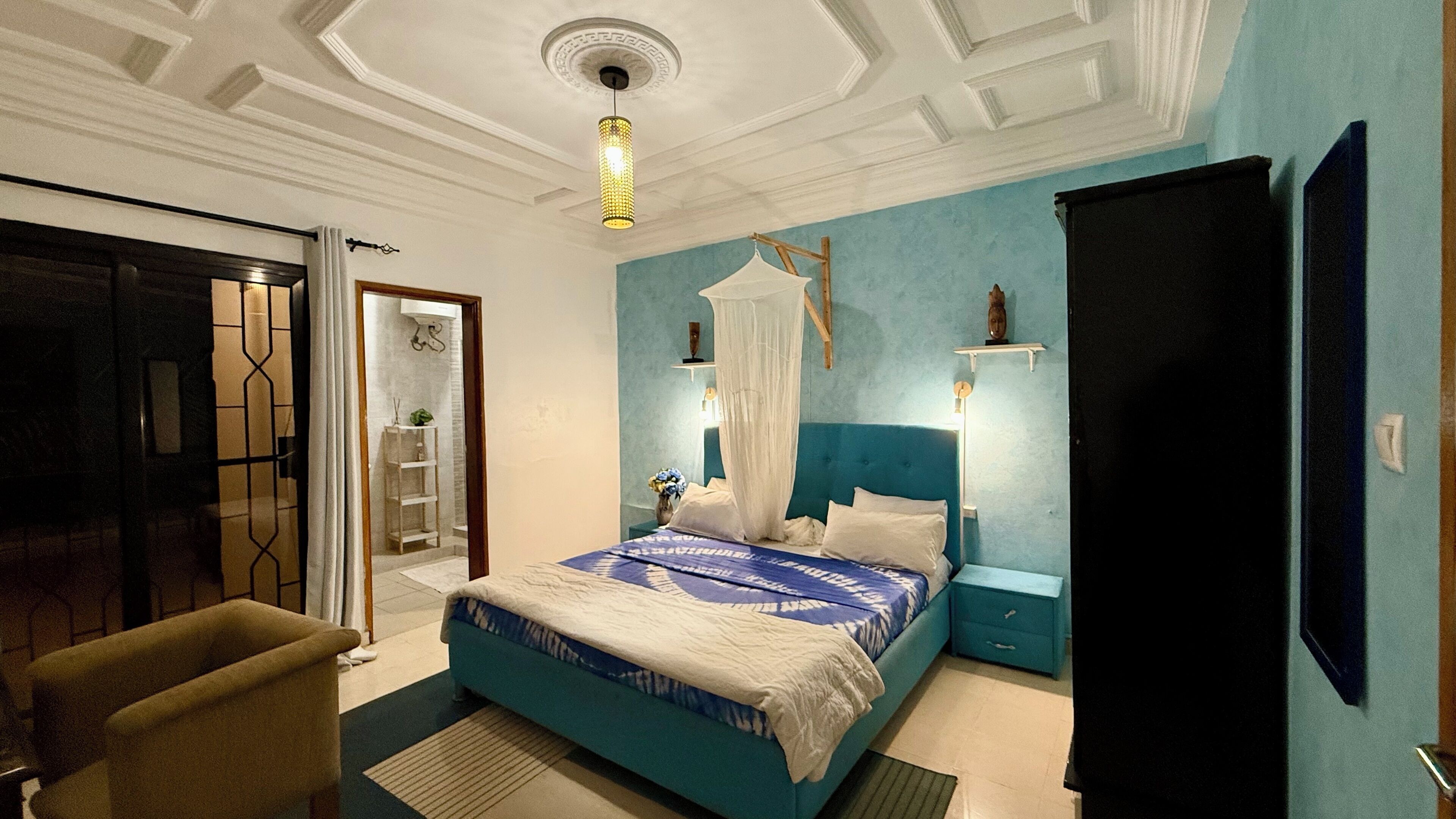 A bedroom with a bed, bedside tables, a chair, a wardrobe, and a ceiling light fixture.