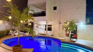 An outdoor swimming pool with lounge chairs, potted plants, and string lights. - Villa Jade (Dakar)