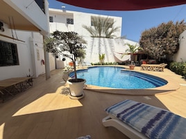Una piscina con sillones de descanso, un árbol en maceta y un extintor en la pared.
