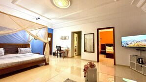 Camera d'albergo con un letto, una scrivania, una sedia, una televisione e un bagno visibile attraverso una porta aperta.