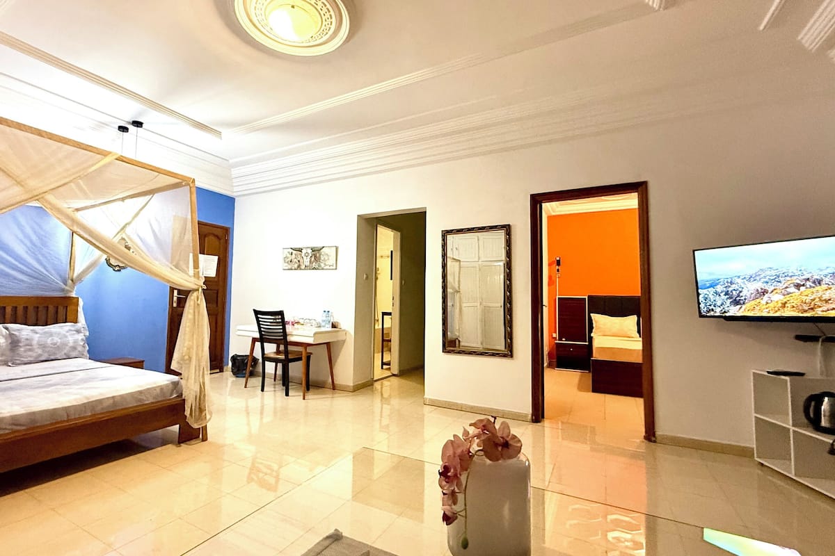 A hotel room with a bed, a desk, a chair, a TV, and a bathroom visible through an open door.