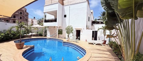 A swimming pool with a sunshade, lounge chairs, and a potted plant.