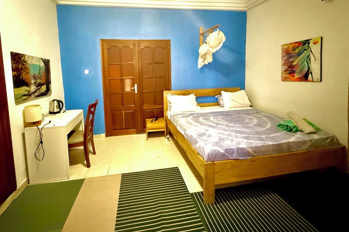 A bedroom with a bed, a desk, a chair, a door, and a painting on the wall.