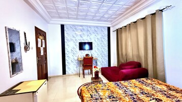 Habitación de hotel con cama, escritorio, silla, televisor y ventana con cortinas.