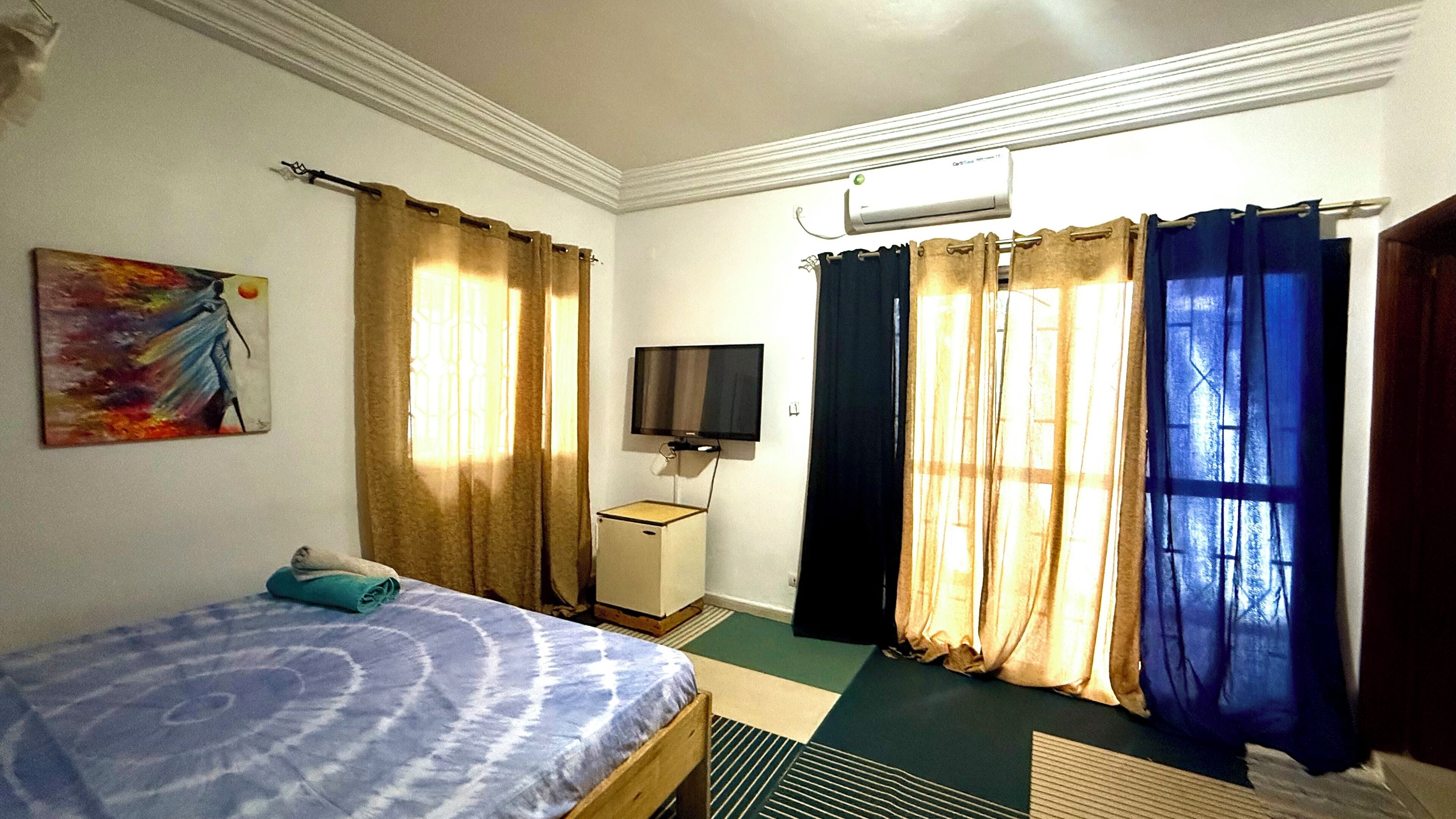 A hotel room with a bed, a TV, a painting, and curtains.