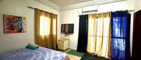 A hotel room with a bed, a TV, a painting, and curtains.