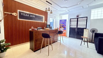 Zona de recepción con mostrador de madera, dos taburetes de bar, un letrero que dice 'VILLA JADE' y una verja negra con diseño decorativo.