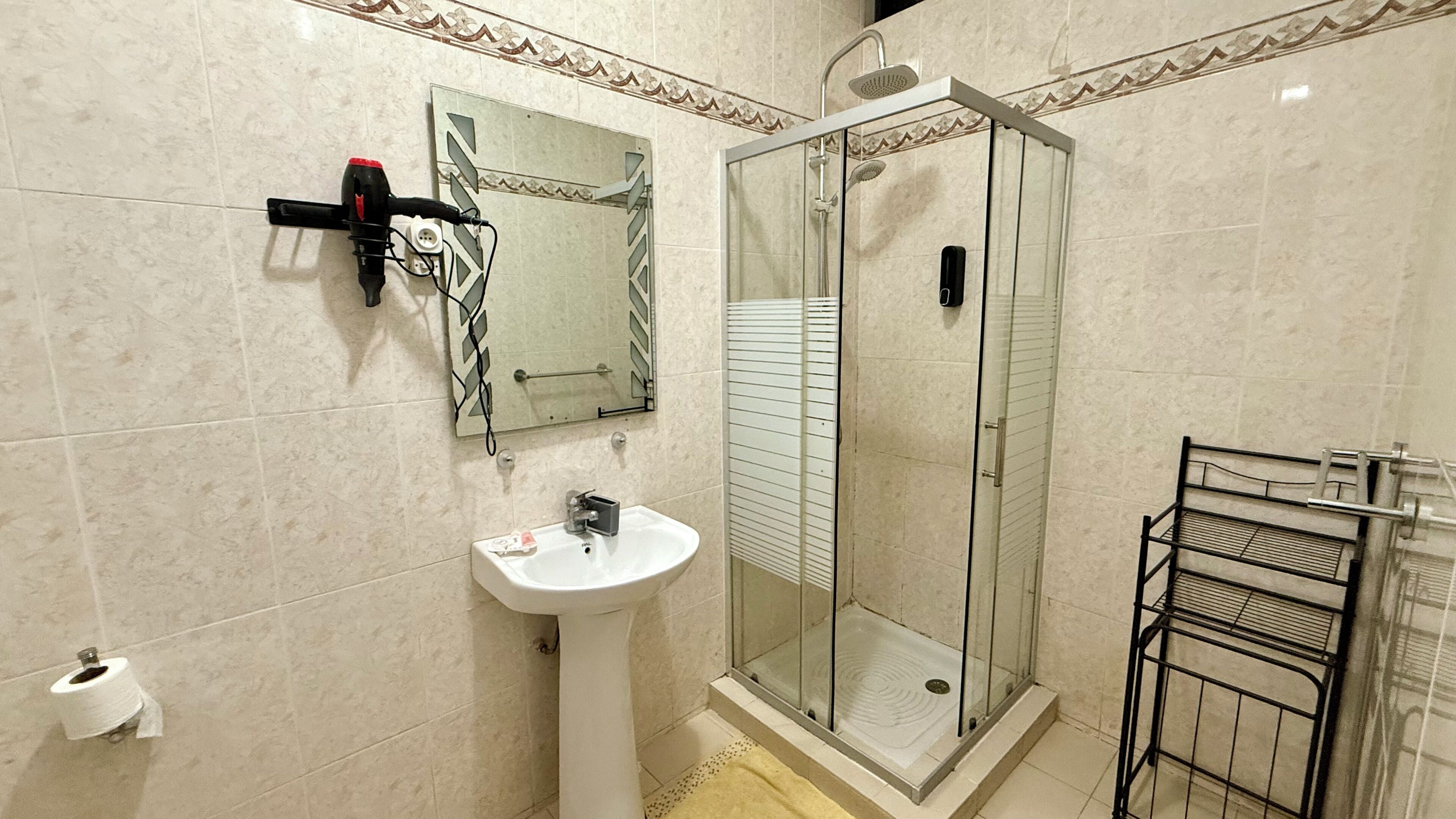 A bathroom with a glass-enclosed shower, a sink, a towel rack, and a toilet paper holder.