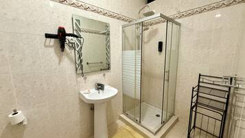 A bathroom with a glass-enclosed shower, a sink, a towel rack, and a toilet paper holder.