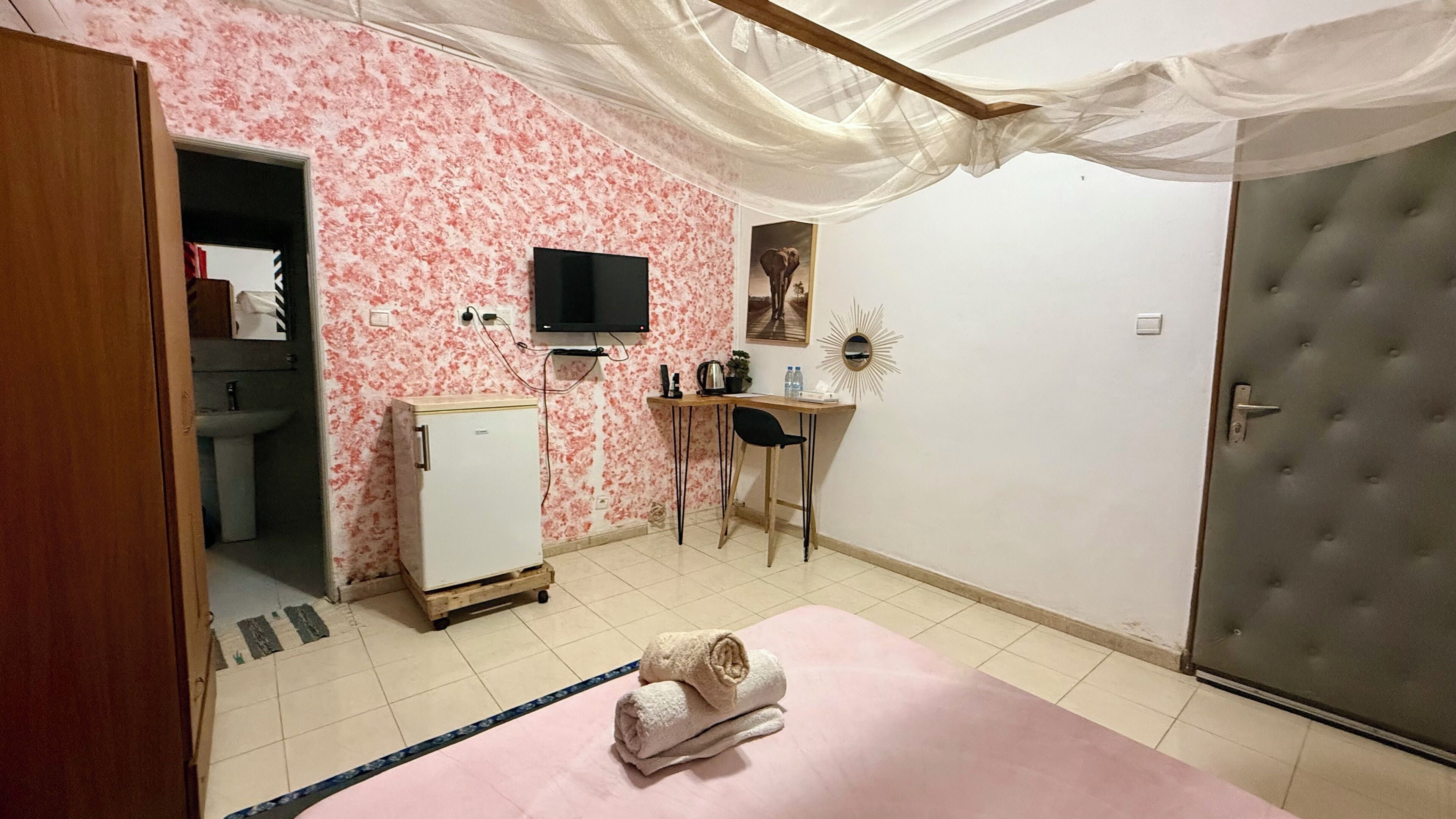 A bedroom with a bed, a desk, a chair, a wardrobe, a television, and a small refrigerator.