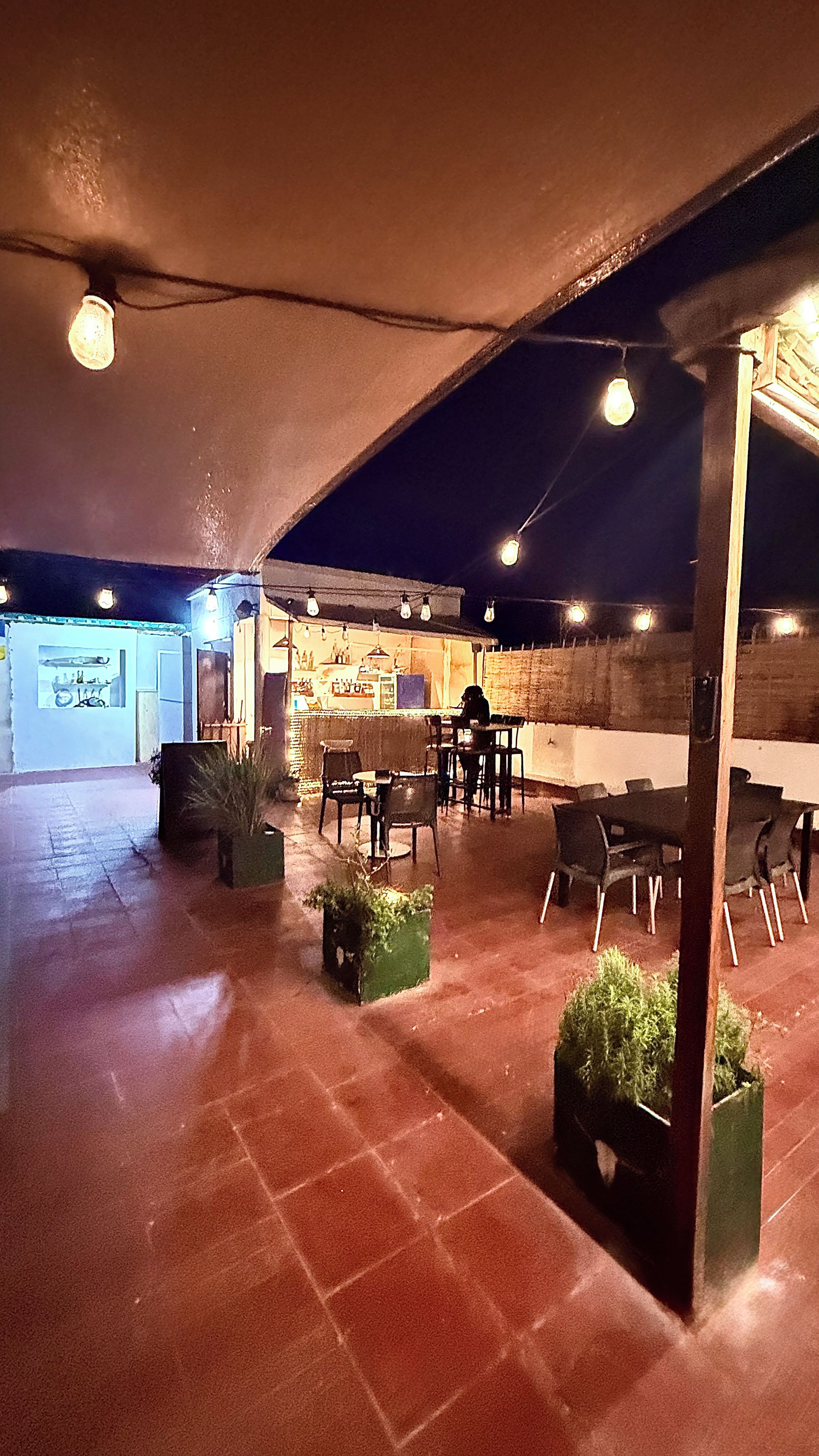 Un área de estar interior con mesas y sillas, una zona de bar con taburetes y una barra.