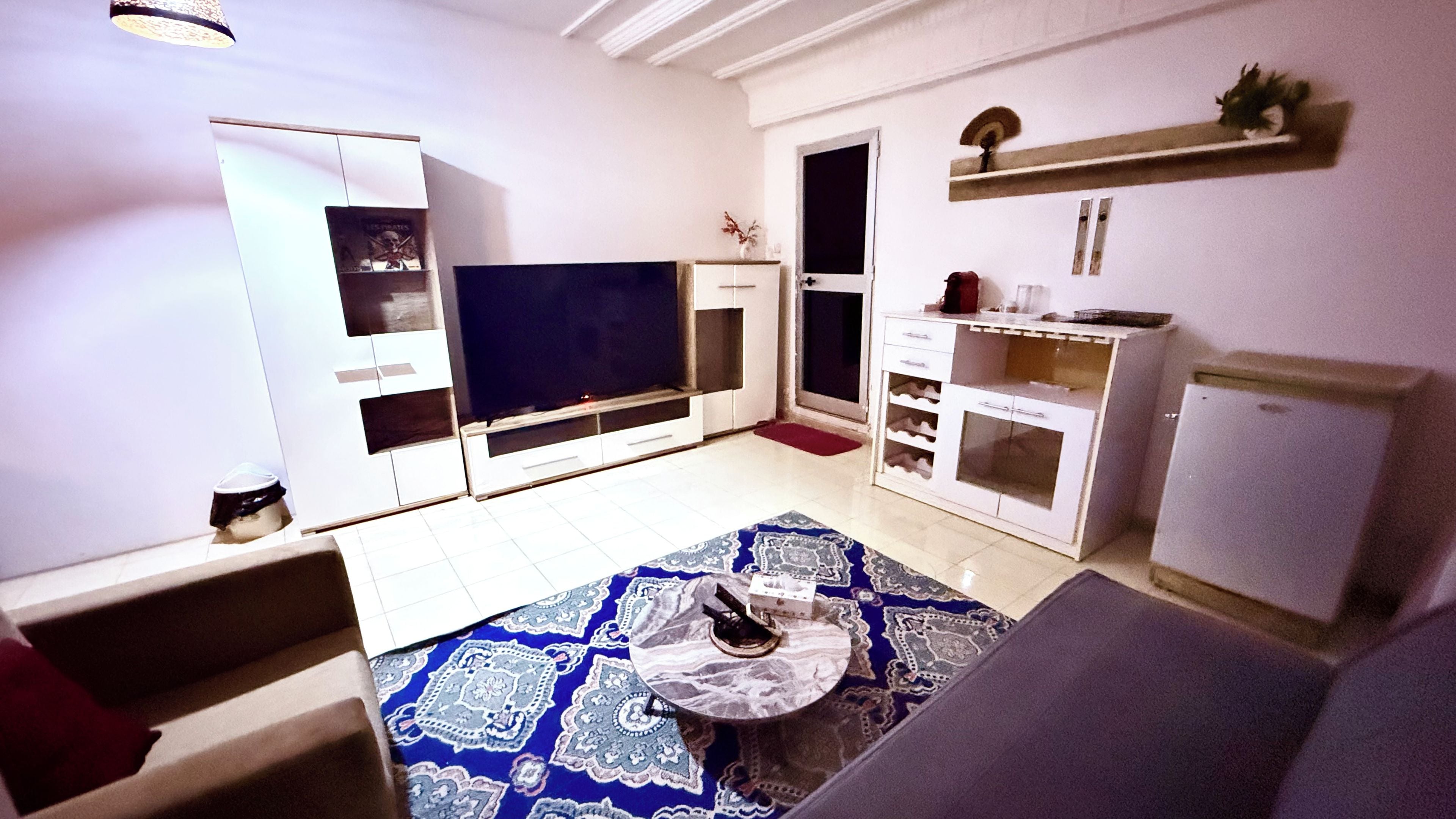 A living room with a flat-screen TV, a sofa, a coffee table, and a patterned rug.