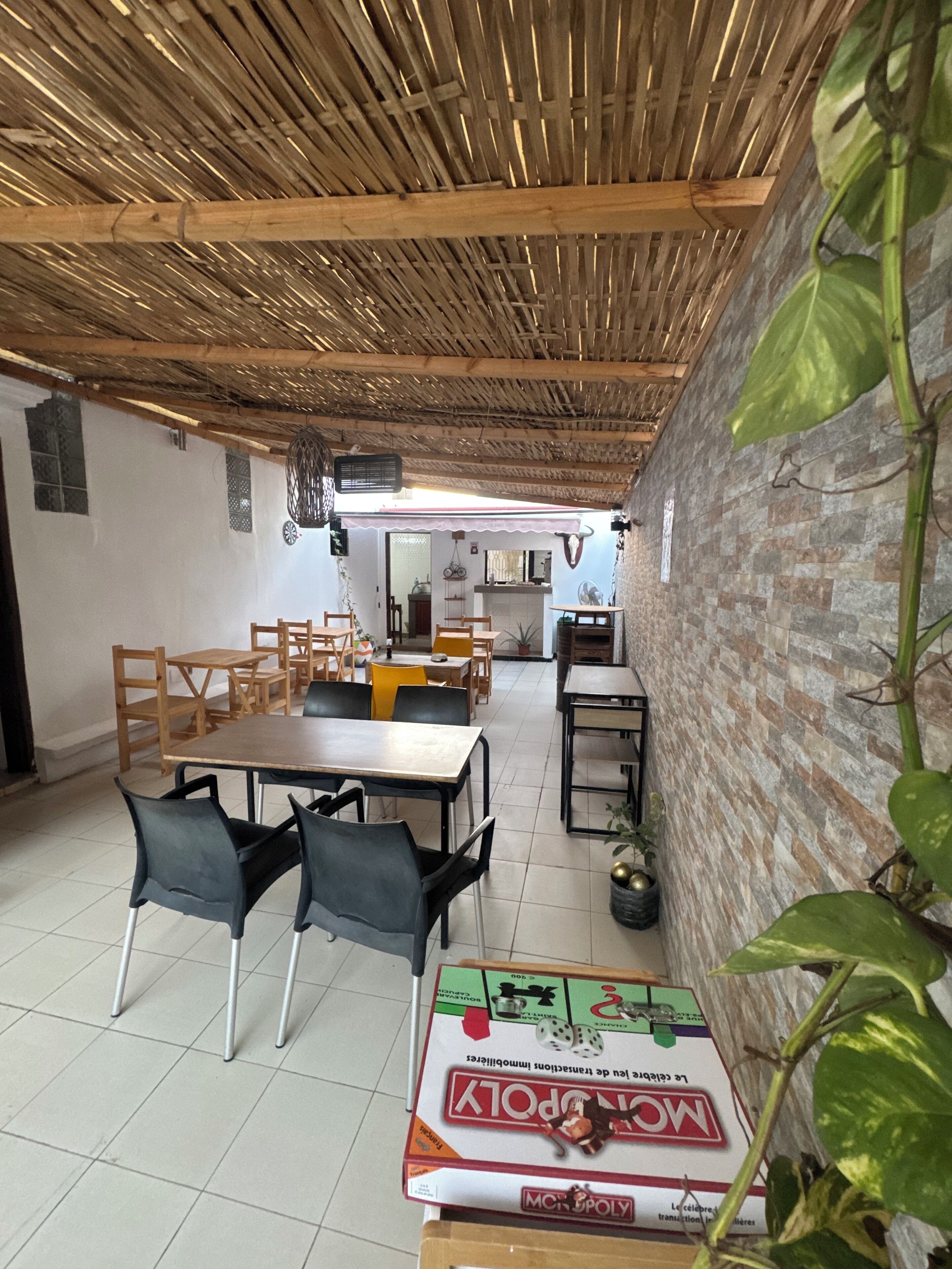 A dining area with wooden tables and chairs, a thatched ceiling, and a brick wall.