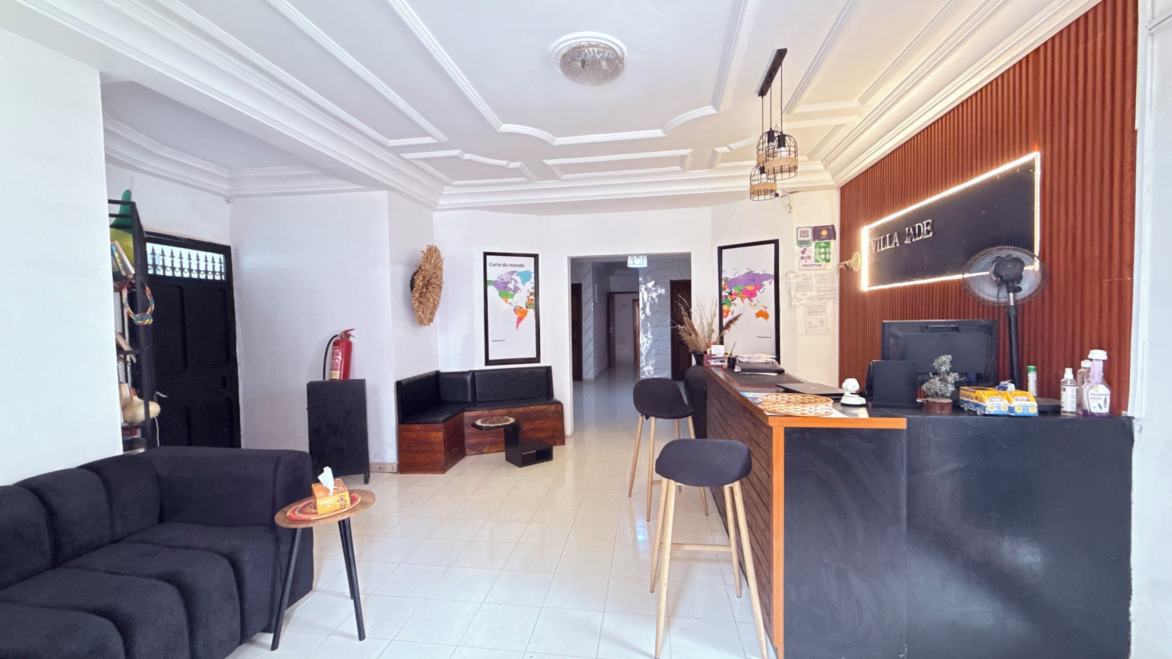A reception area with a wooden reception desk, black chairs, a black sofa, and a white ceiling with decorative molding.