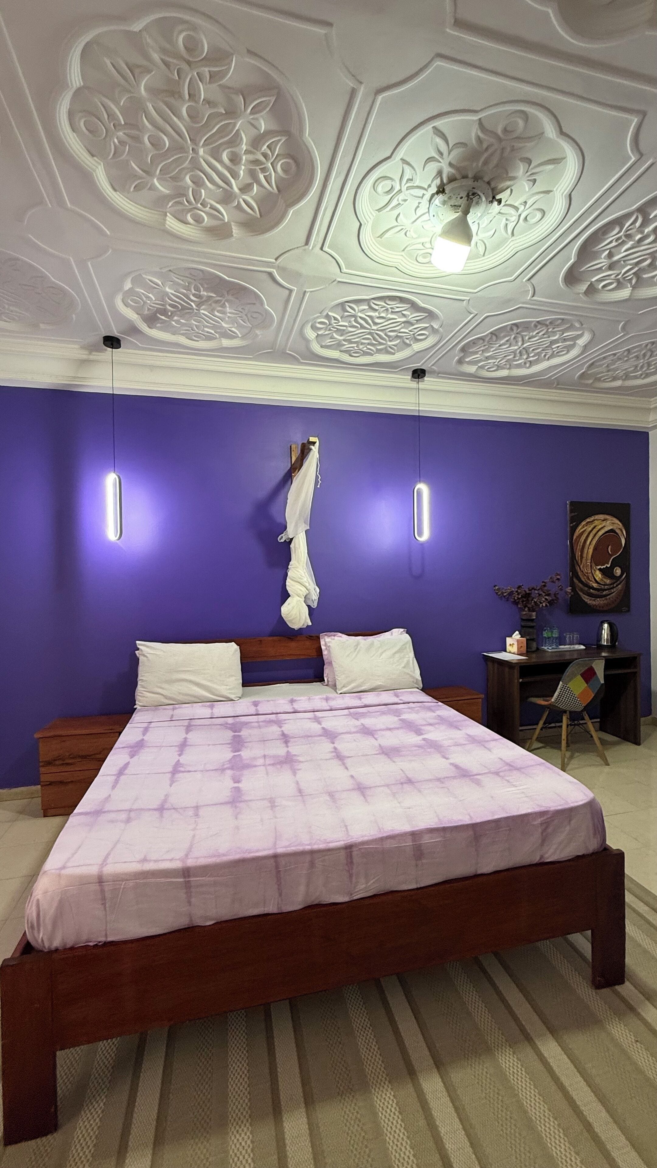 Een slaapkamer met een paarse muur, een houten bed en een plafond met ingewikkelde decoraties.