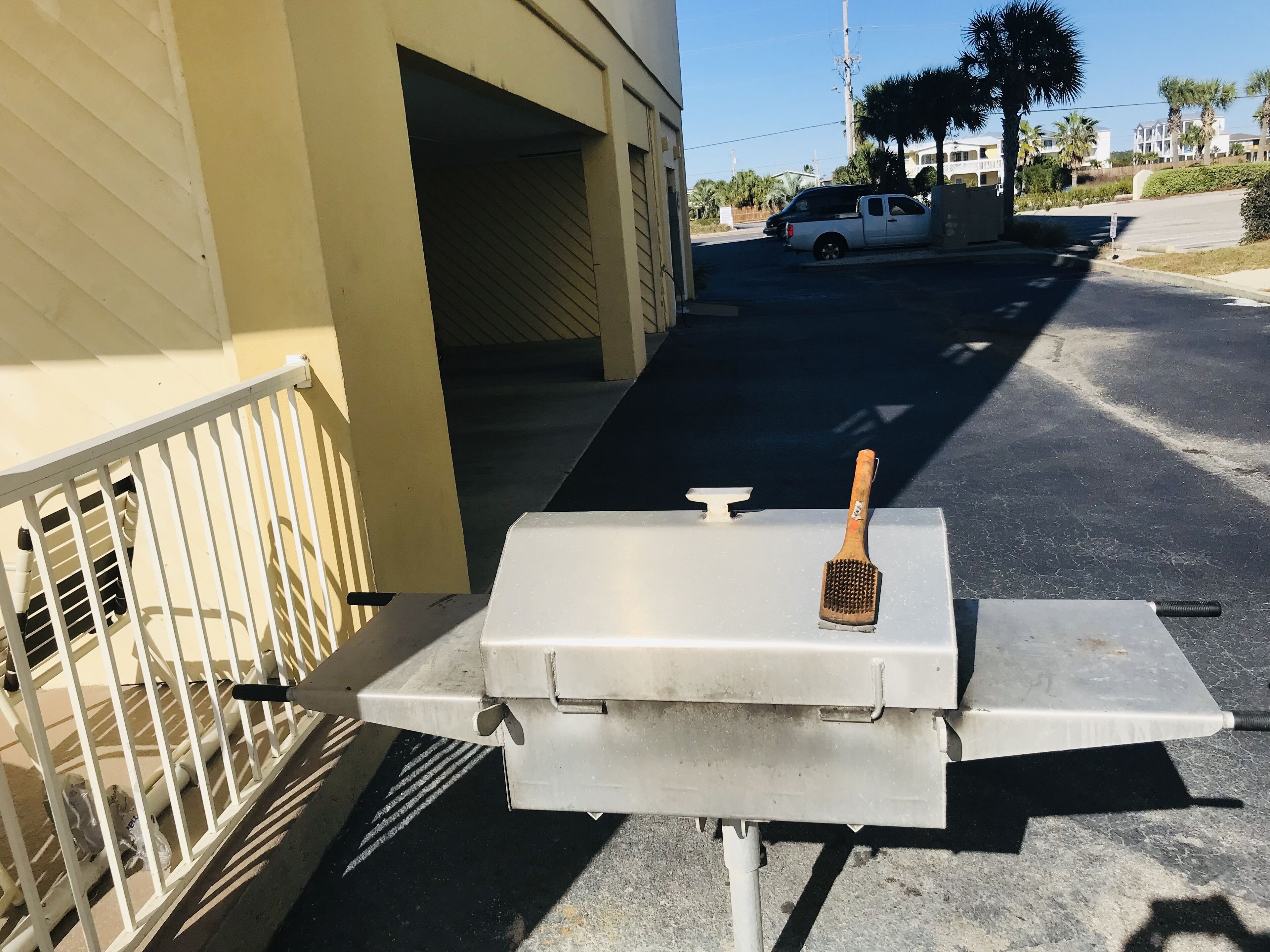 A grill with a brush on a metal stand in a parking lot.