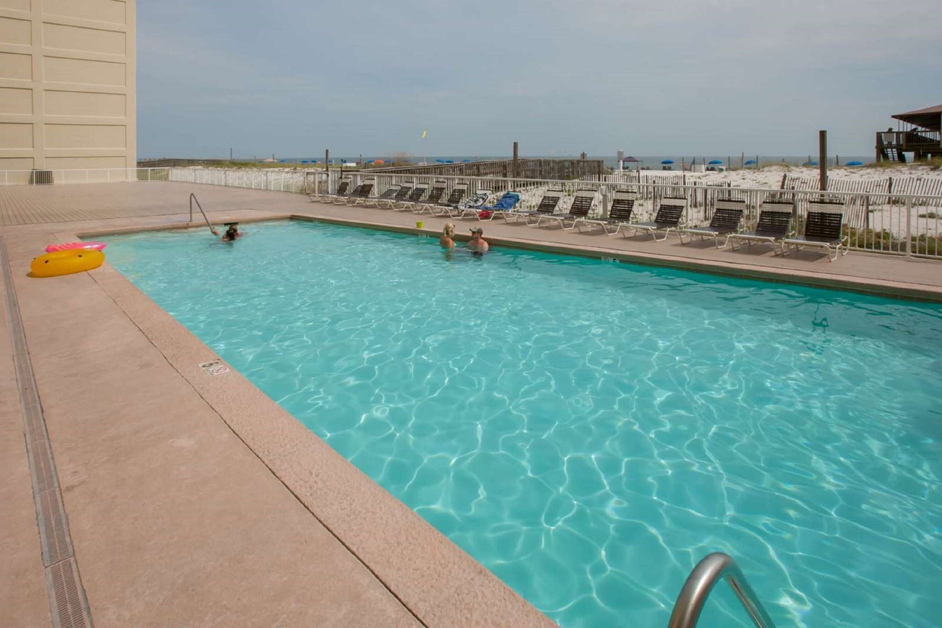 Una piscina con acqua cristallina, una sedia per il bagnino e lettini a bordo vasca.