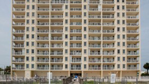 A multi-story hotel with a uniform exterior, balconies on each floor, and a sandy beach area in front. - Boardwalk Condos by Hosteeva (Gulf Shores)