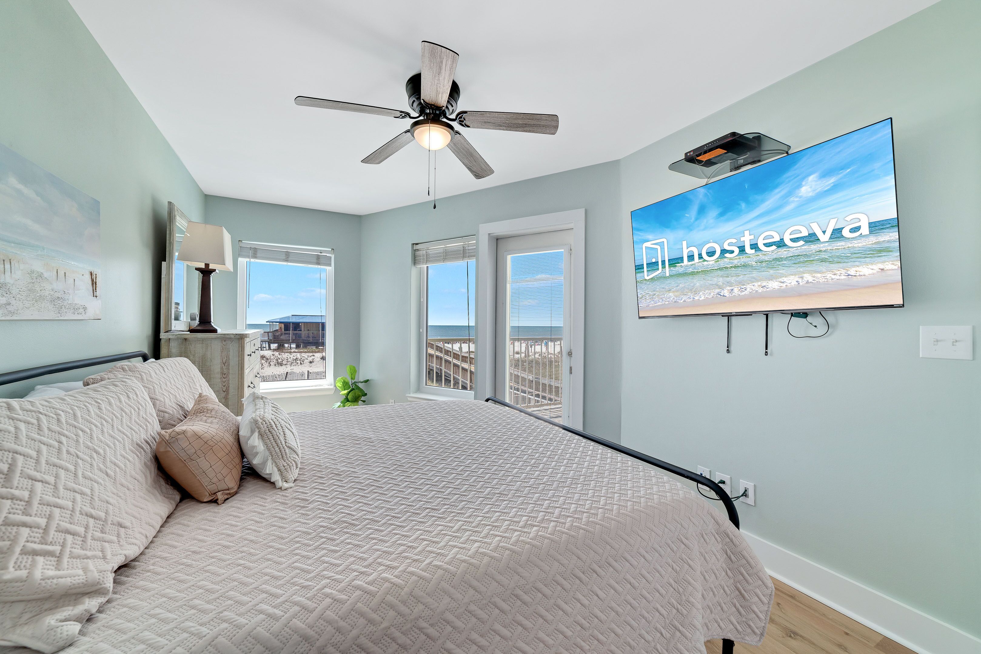Une chambre avec un lit, un ventilateur de plafond, une télévision et une vue sur la plage.