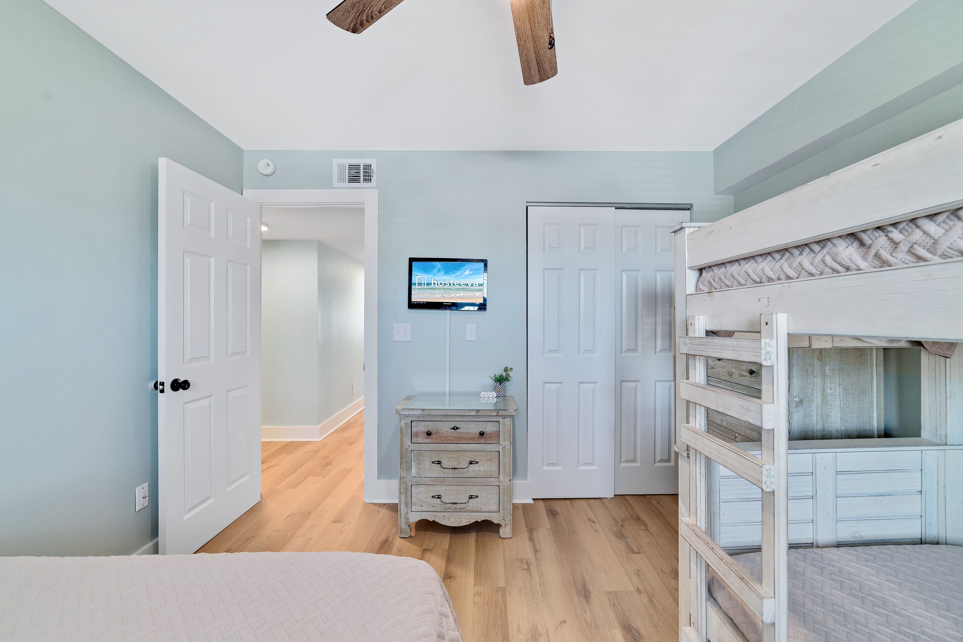 A bedroom with a bunk bed, a dresser, a television, and a door leading to another room.
