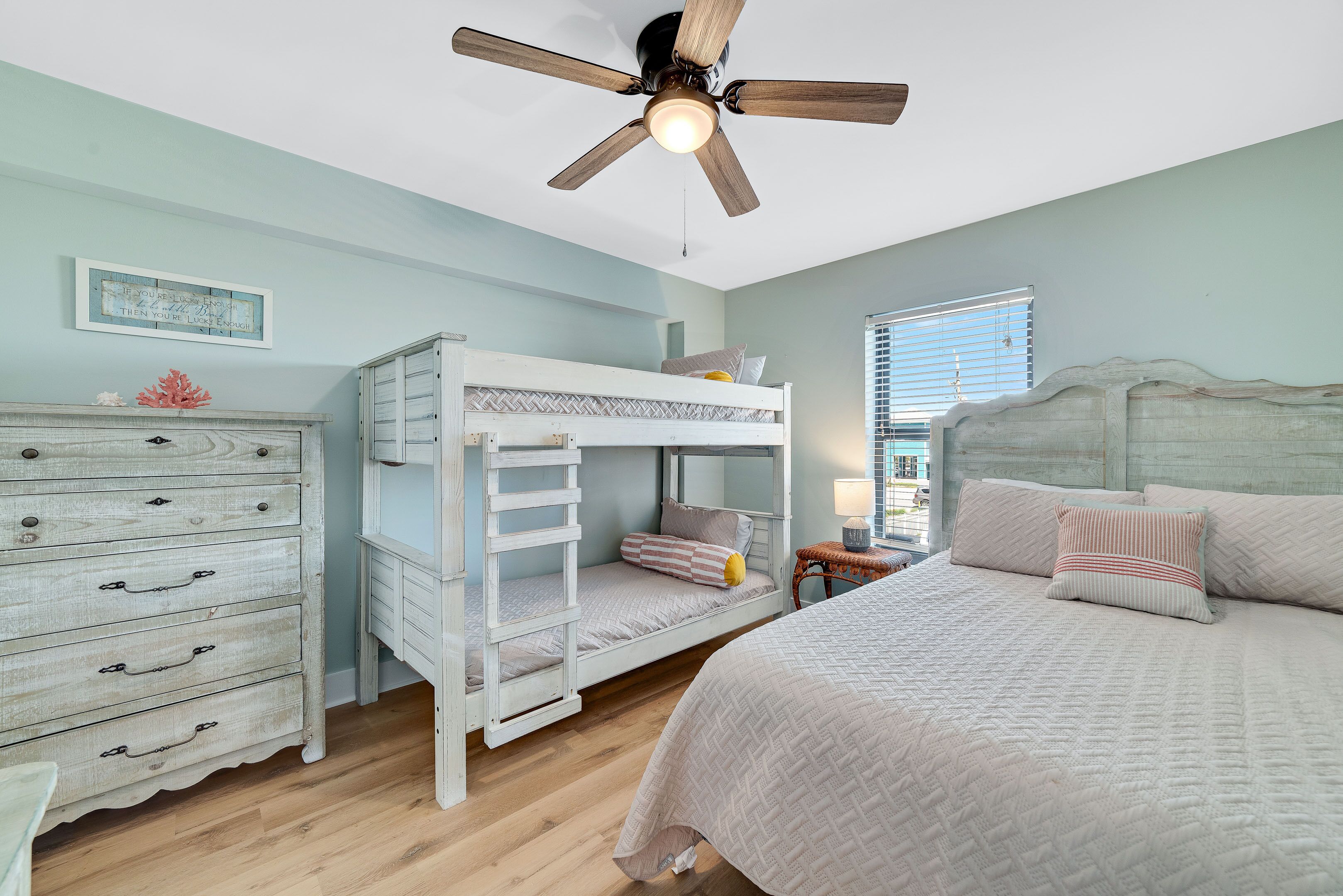 A bedroom with a bunk bed, a dresser, a ceiling fan, and a window with blinds.