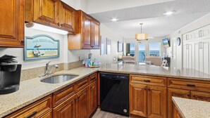 A kitchen with wooden cabinets, a built-in dishwasher, and a granite countertop. - Boardwalk Condos by Hosteeva (Gulf Shores)