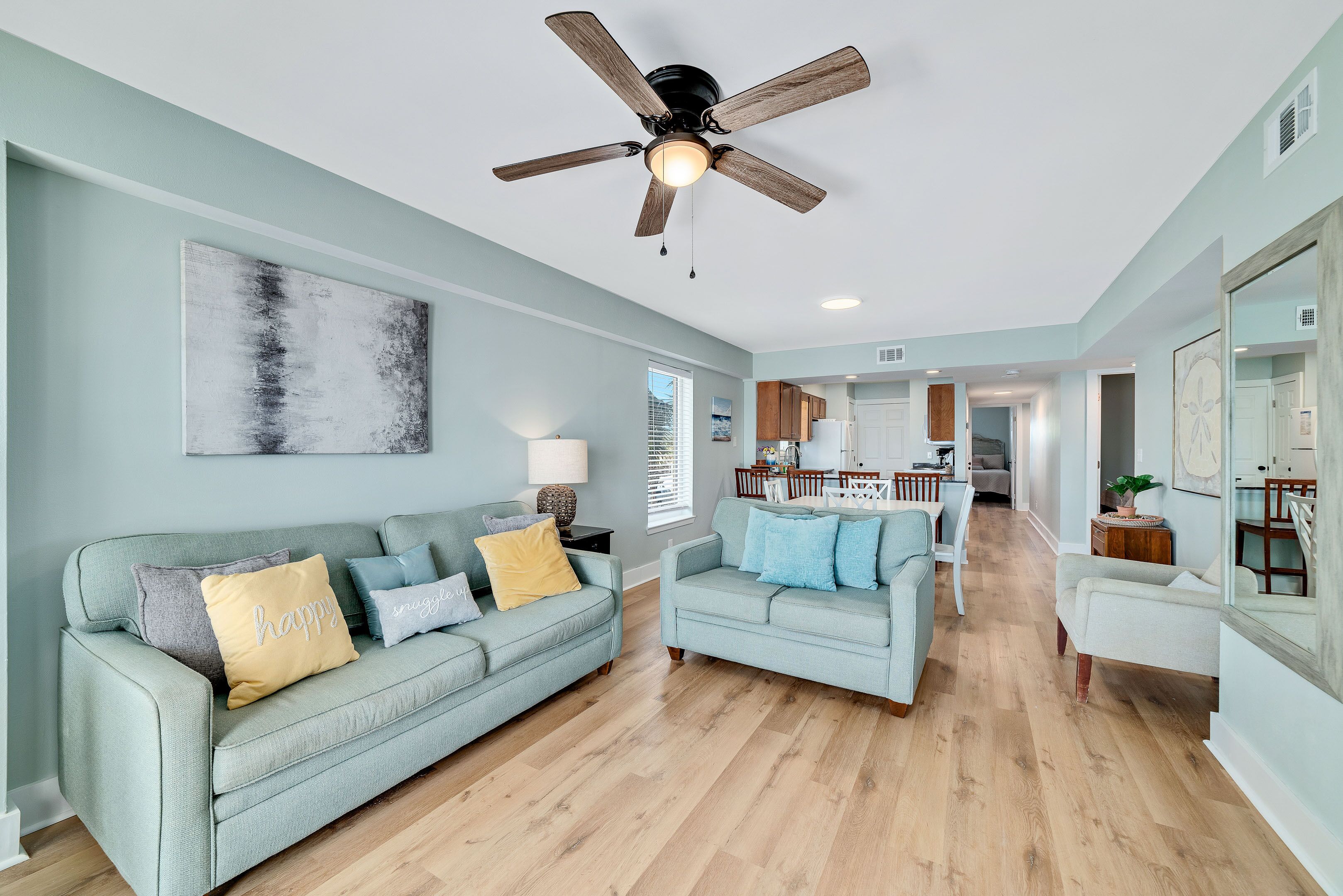 A spacious living room with a ceiling fan, light-colored sofas, and a wooden floor.