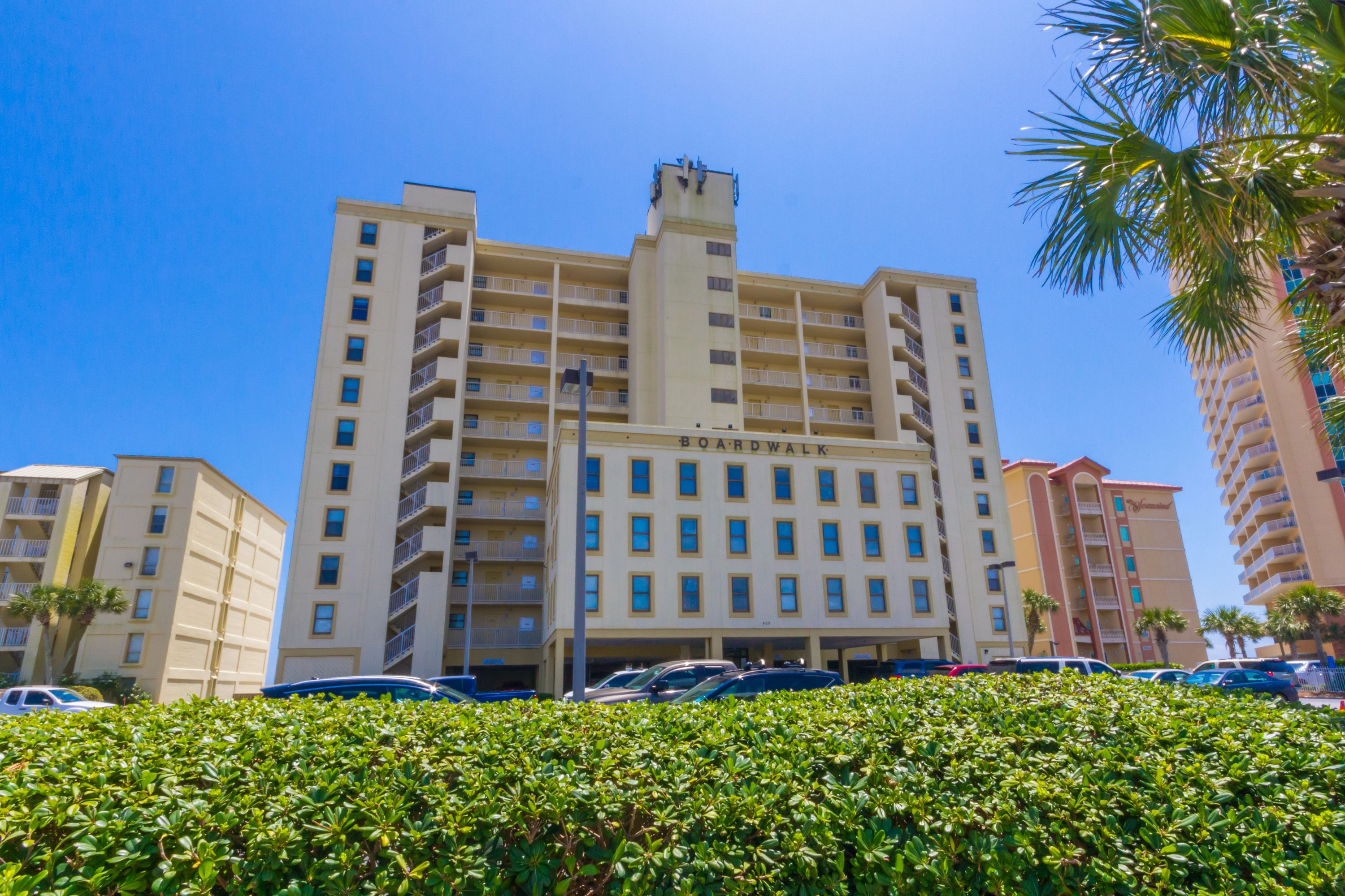 A multi-story hotel with a central tower, multiple balconies, and a parking area in front.