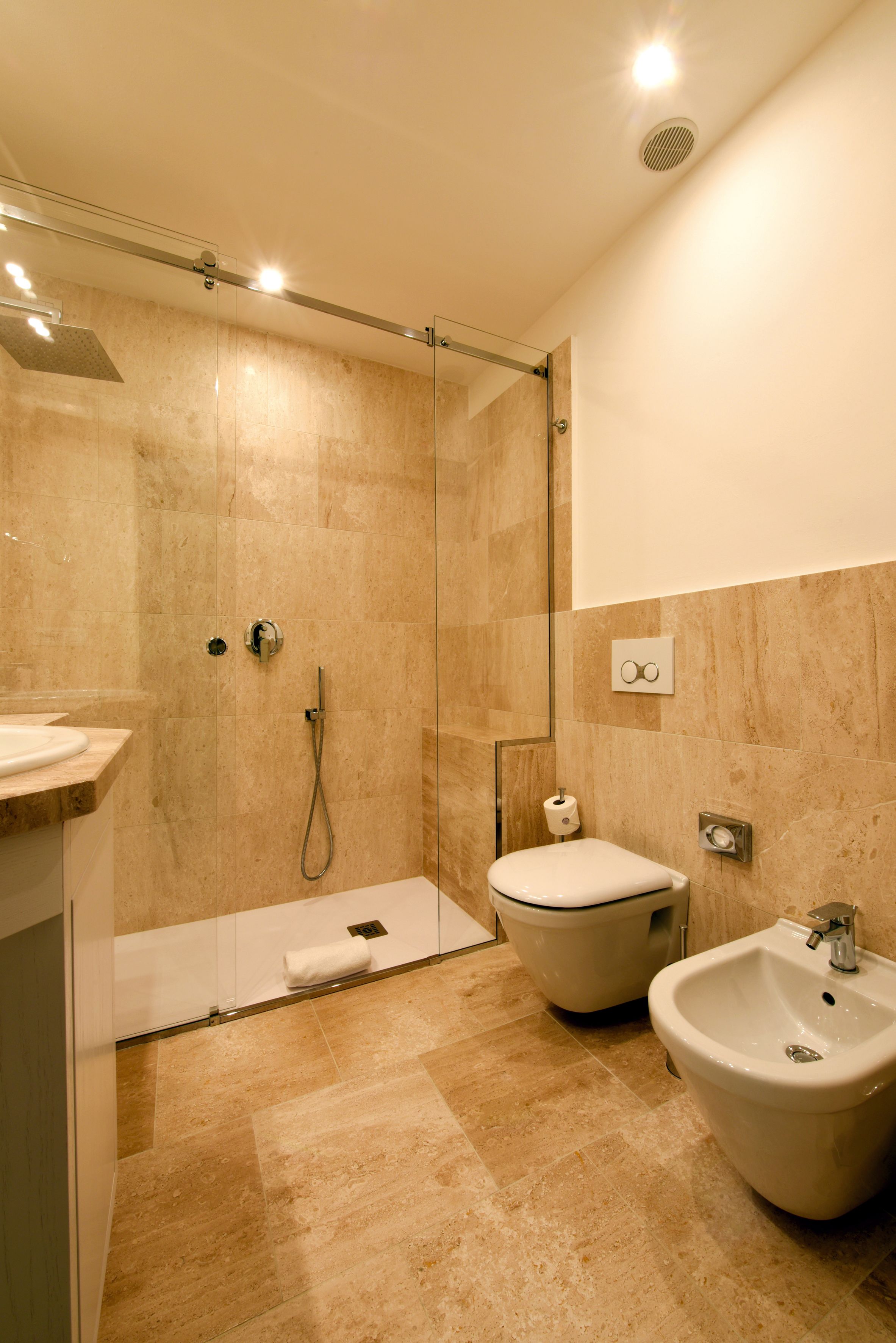 A modern bathroom with a glass-enclosed shower, a toilet, and a bidet.