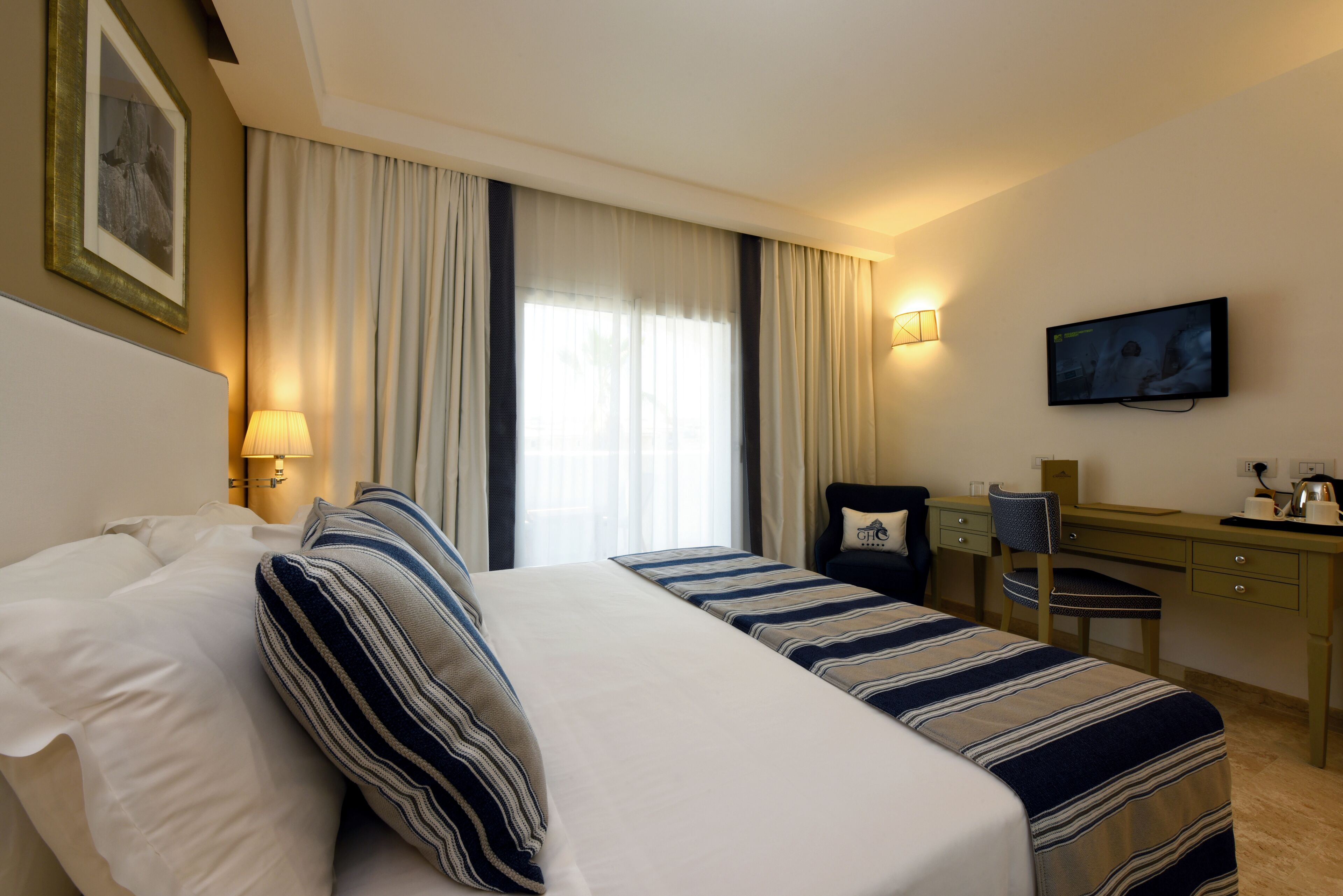 Een hotelkamer met een bed, een bureau, een stoel, een televisie en een raam met gordijnen.