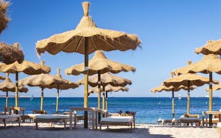 A beach with straw umbrellas and wooden lounge chairs.