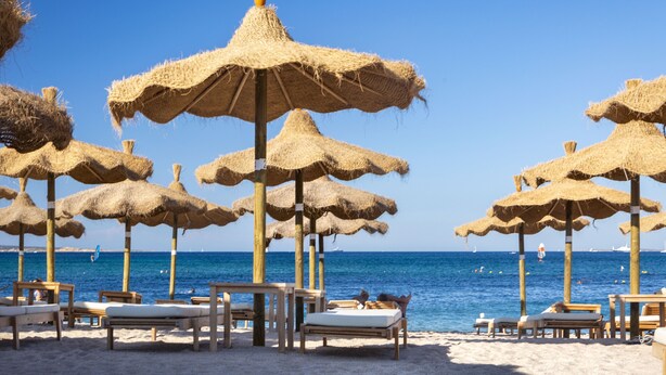 Ein Strand mit Strohdächern und Holzliegestühlen.