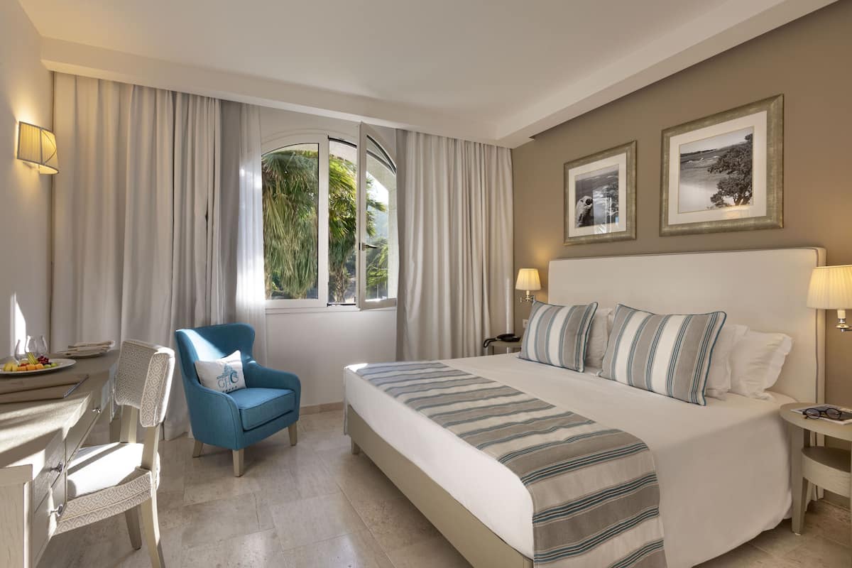 A hotel room with a bed, a chair, a desk, and a window with curtains.