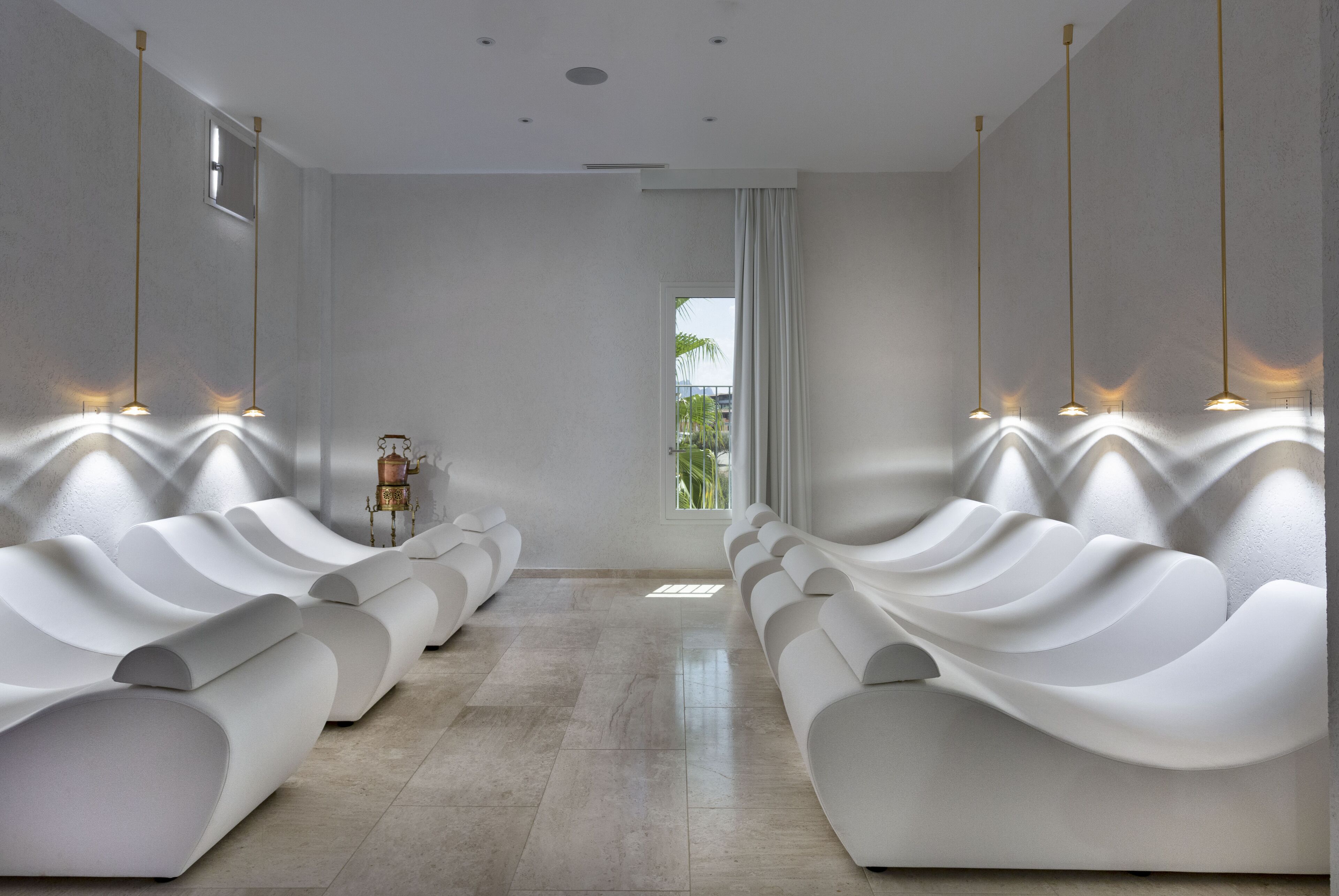 A modern spa room with white, wavy seating and pendant lighting.