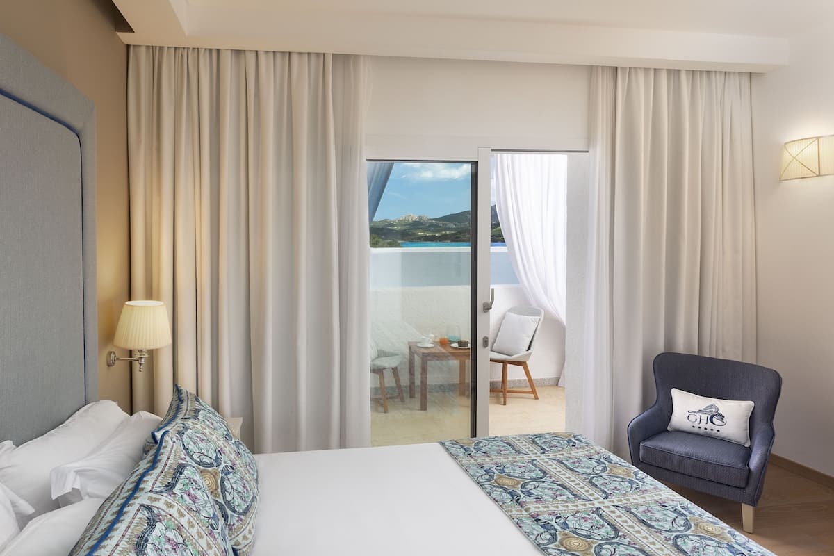 A hotel room with a bed, a chair, a table, and a view of a balcony with a table and chairs.