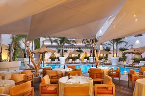 Un espace extérieur aménagé pour les repas, avec des tables et des chaises rondes, une piscine et des parasols.