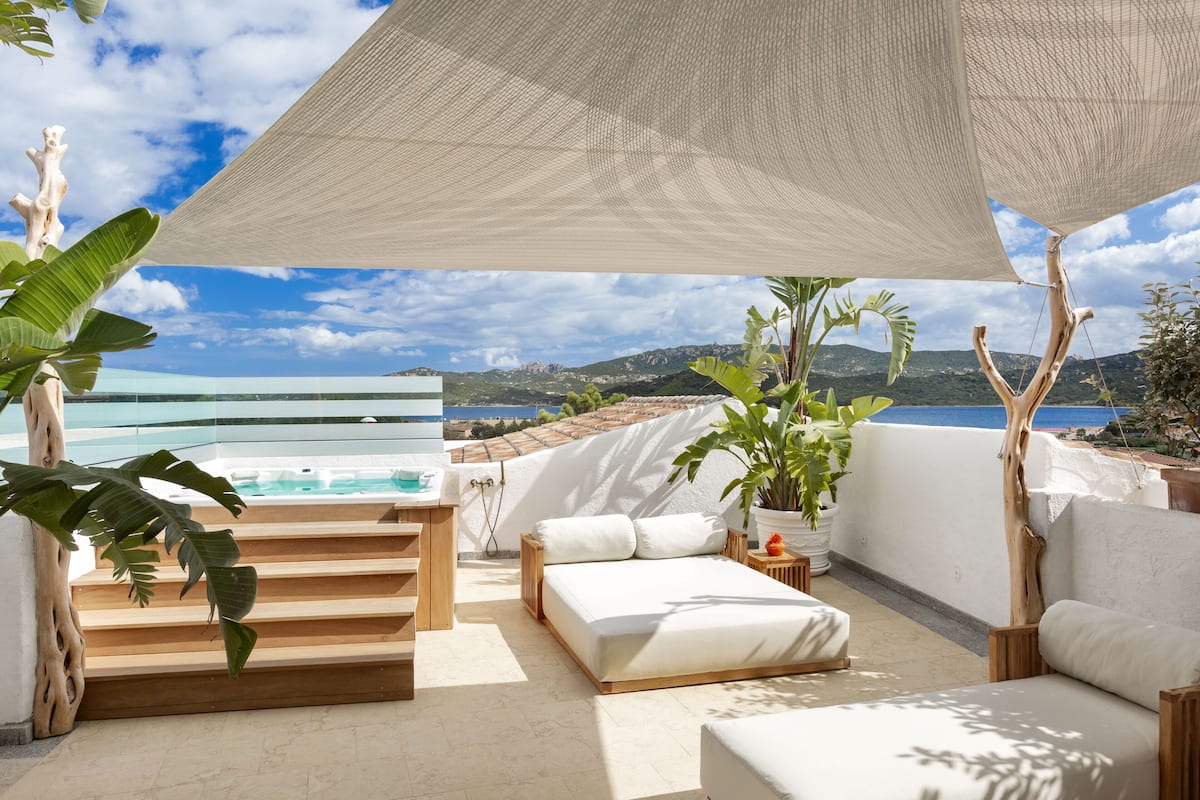 A modern outdoor balcony with a bed, seating area, and a view of the sea.
