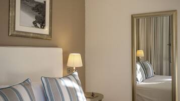 A hotel room with a bed, a nightstand, a lamp, a framed picture on the wall, and a mirror reflecting the bed and lamp.